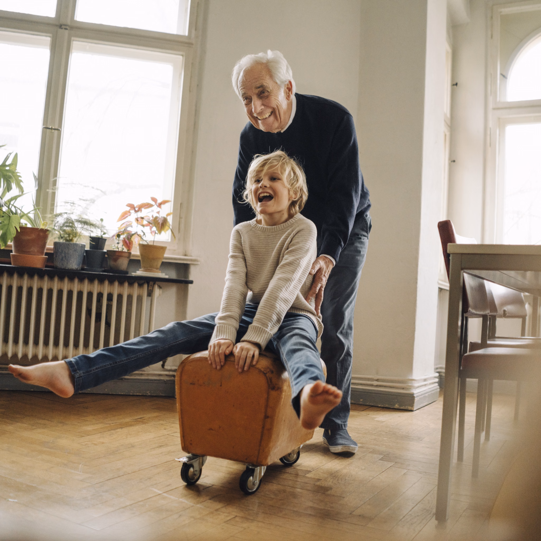 Senior schiebt fröhlich seinen Enkel der auf einem rollenden Hocker sitzt