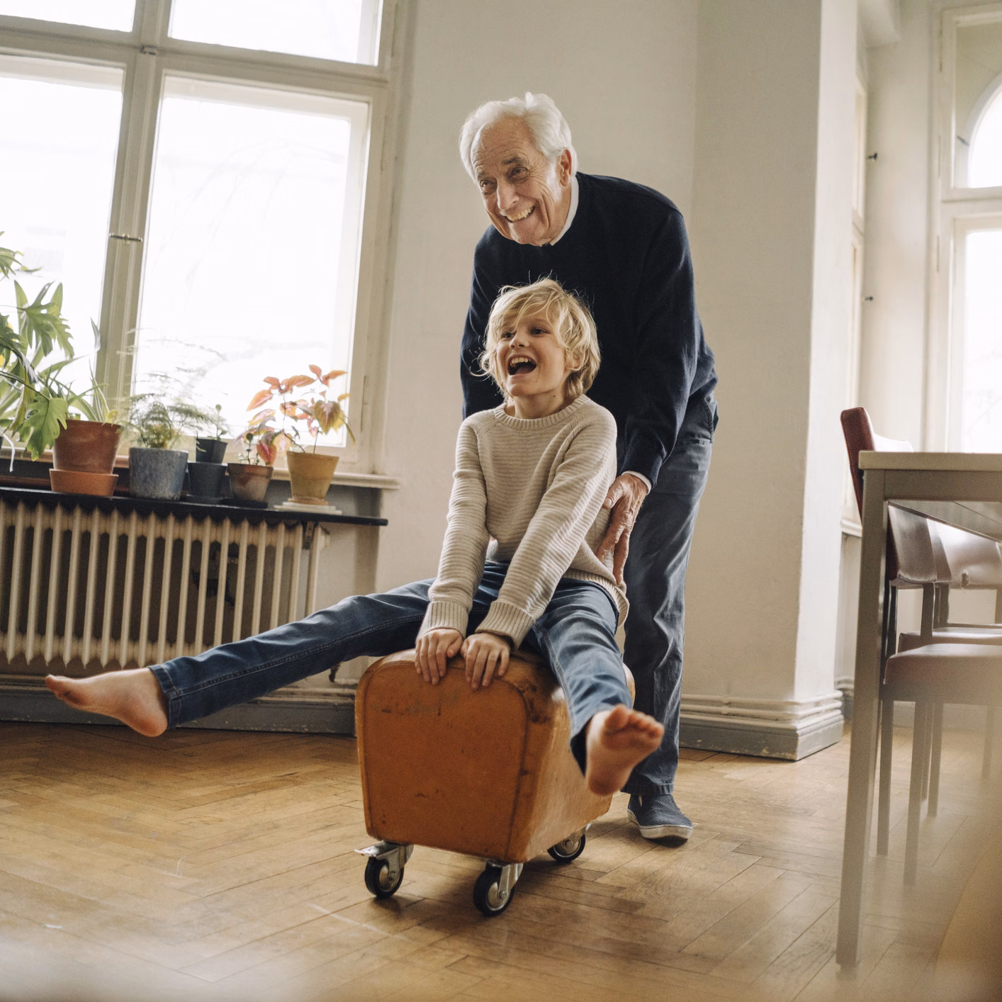 Senior schiebt fröhlich seinen Enkel der auf einem rollenden Hocker sitzt