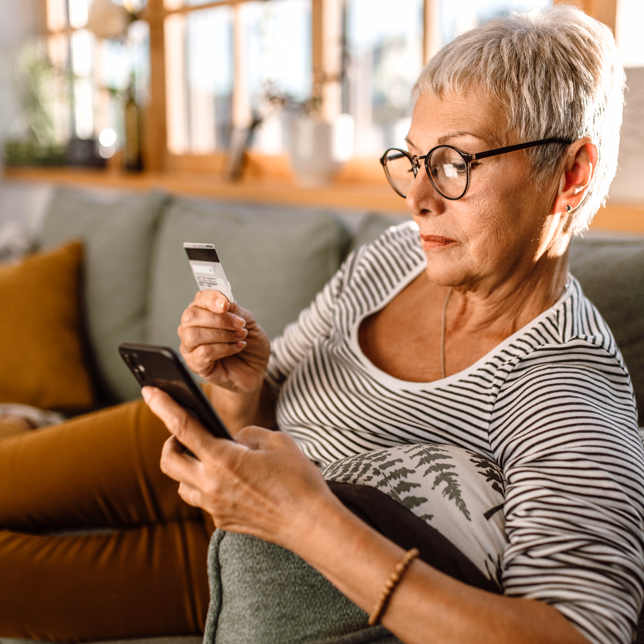 70 jährige Frau liegt auf Couch und hat Versichertenkarte und Handy in den Händen.