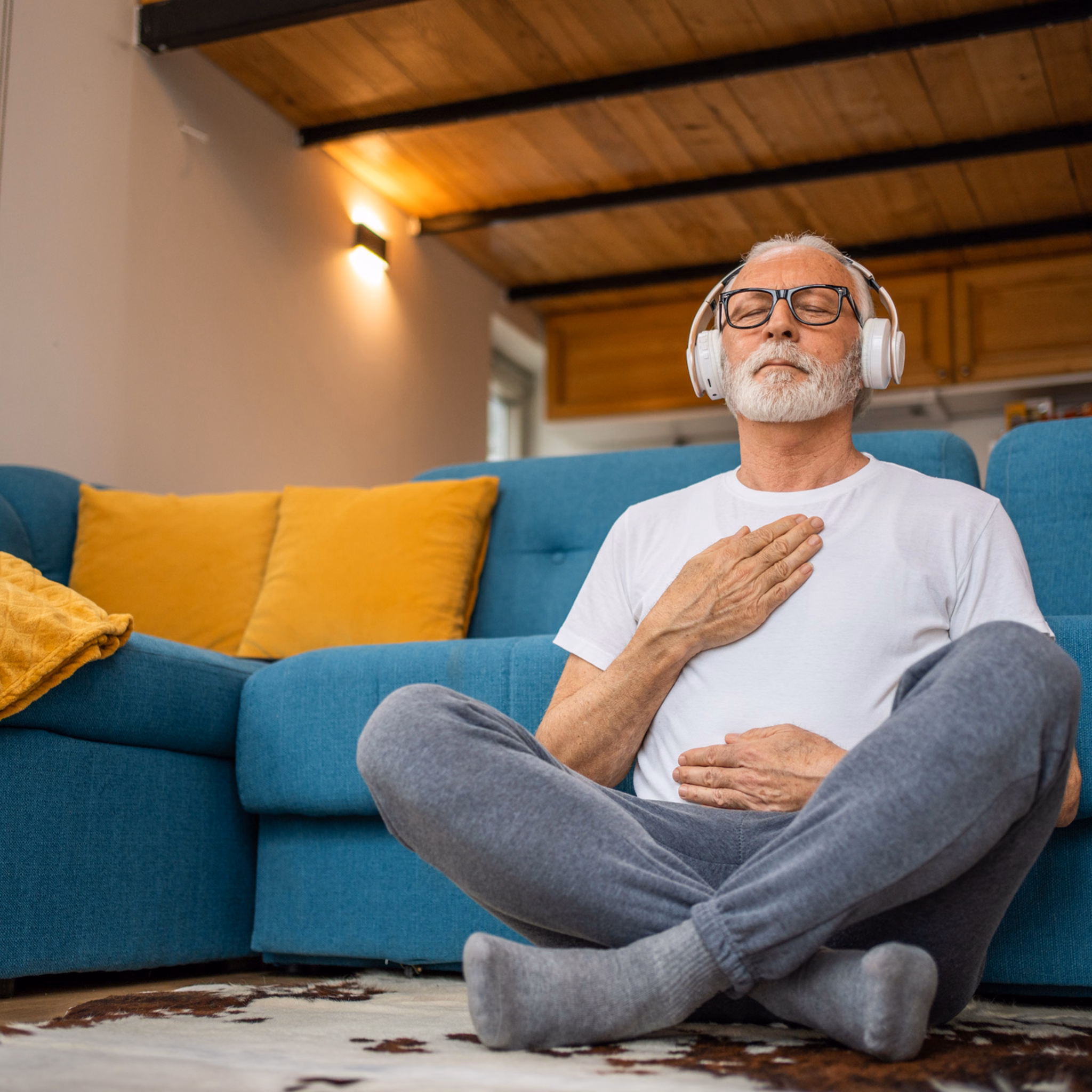70 jähriger Mann sitzt vor Sofa und macht Atemübungen.