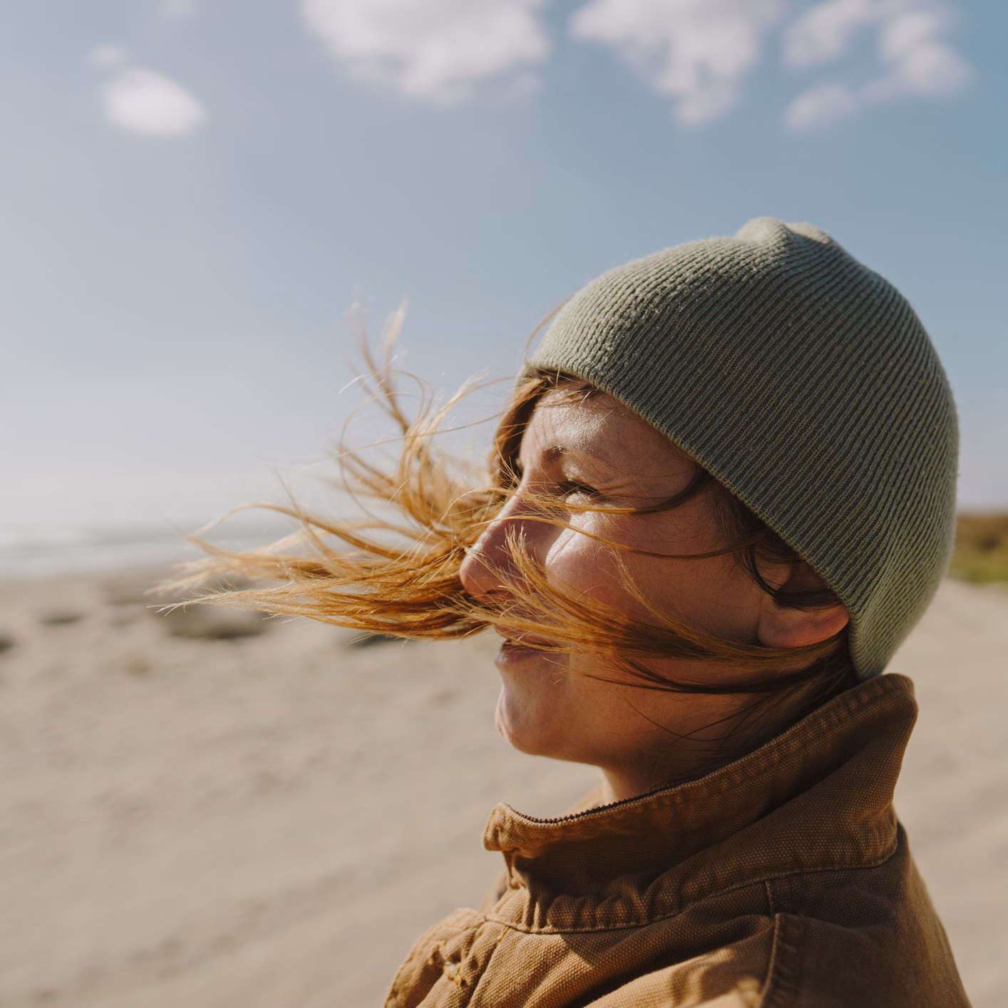 Frau mit Mütze steht am Strand bei Wind