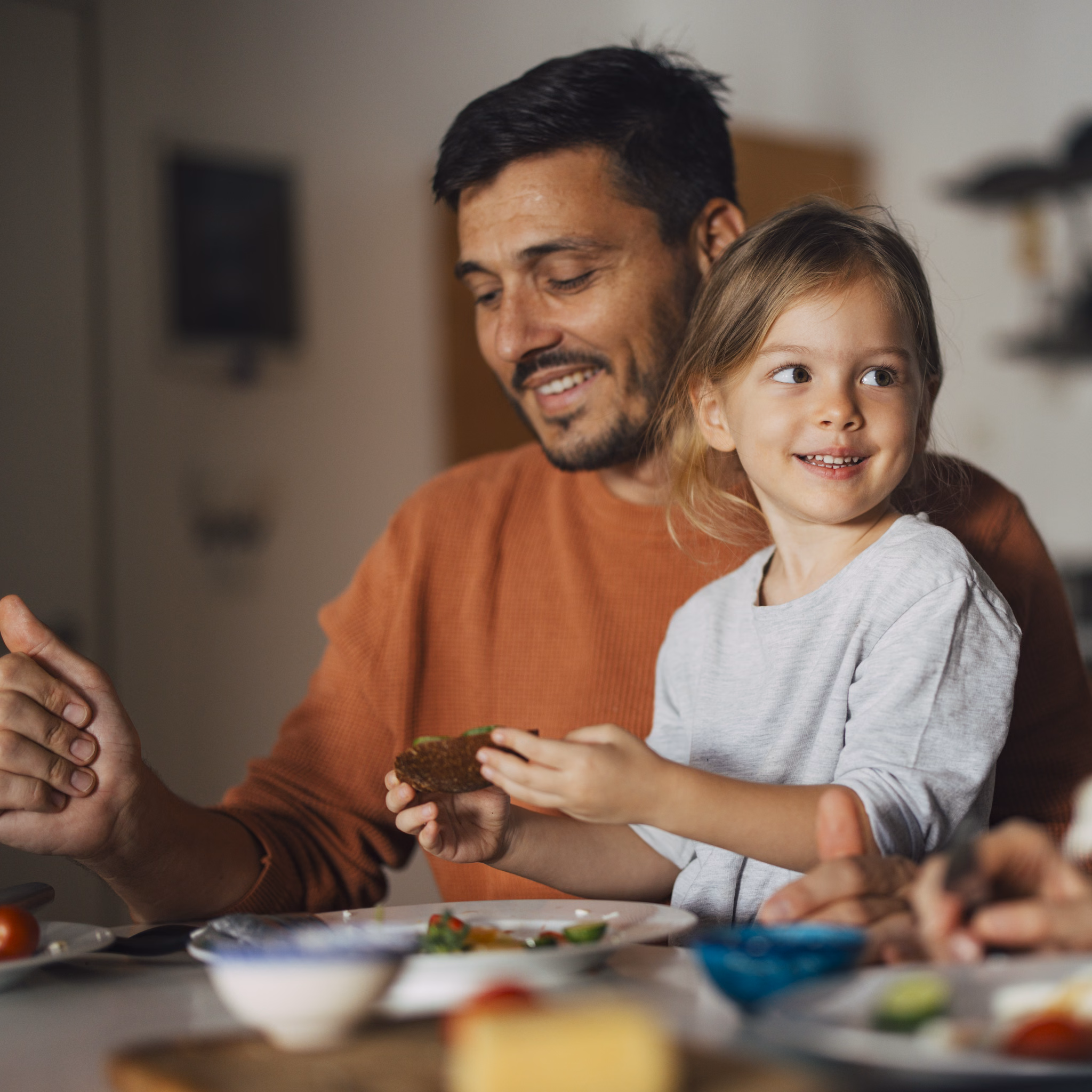 Eltern und Tochter sitzen in Küche und essen.