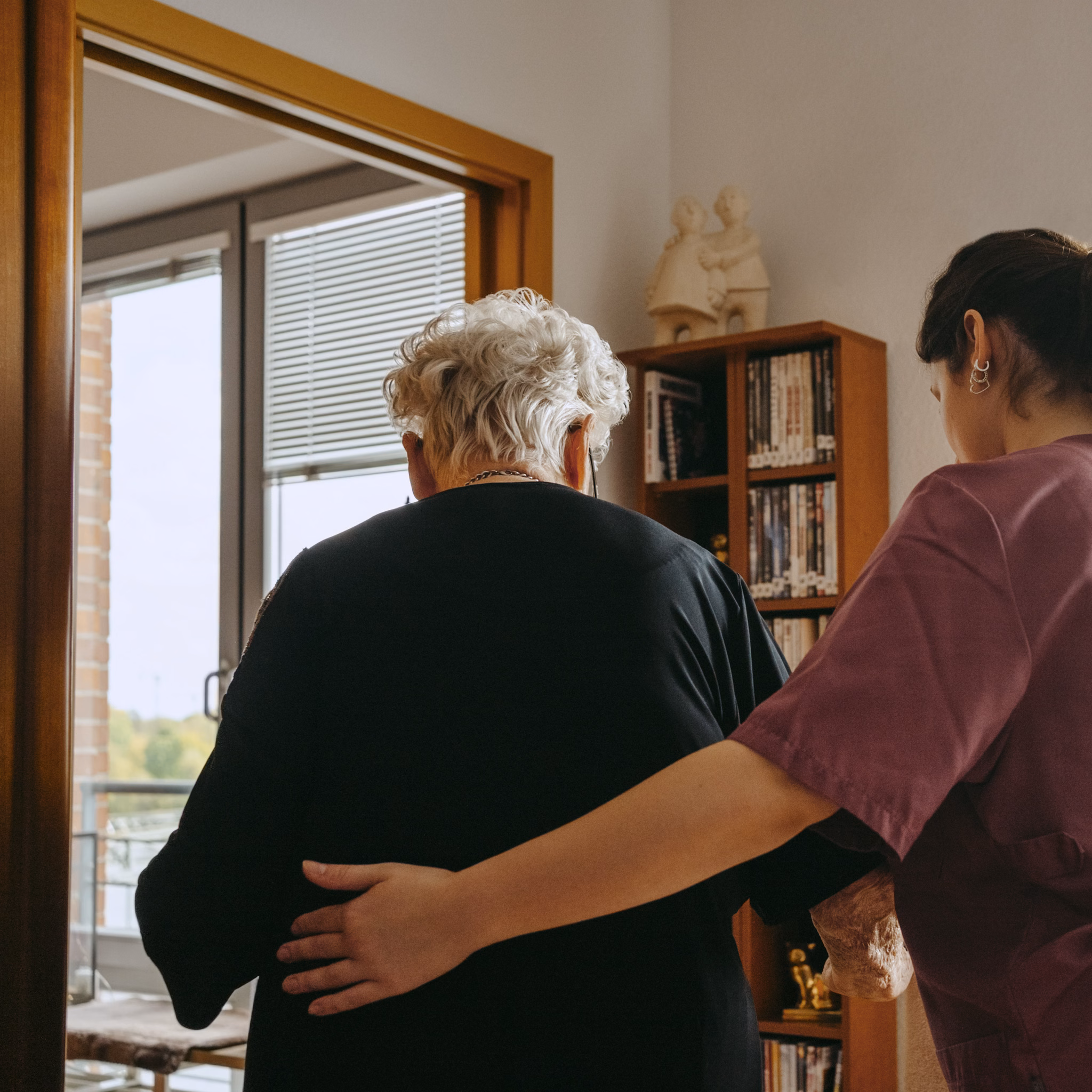 Seniorin wird von weiblicher Pflegekraft am Rücken gestützt