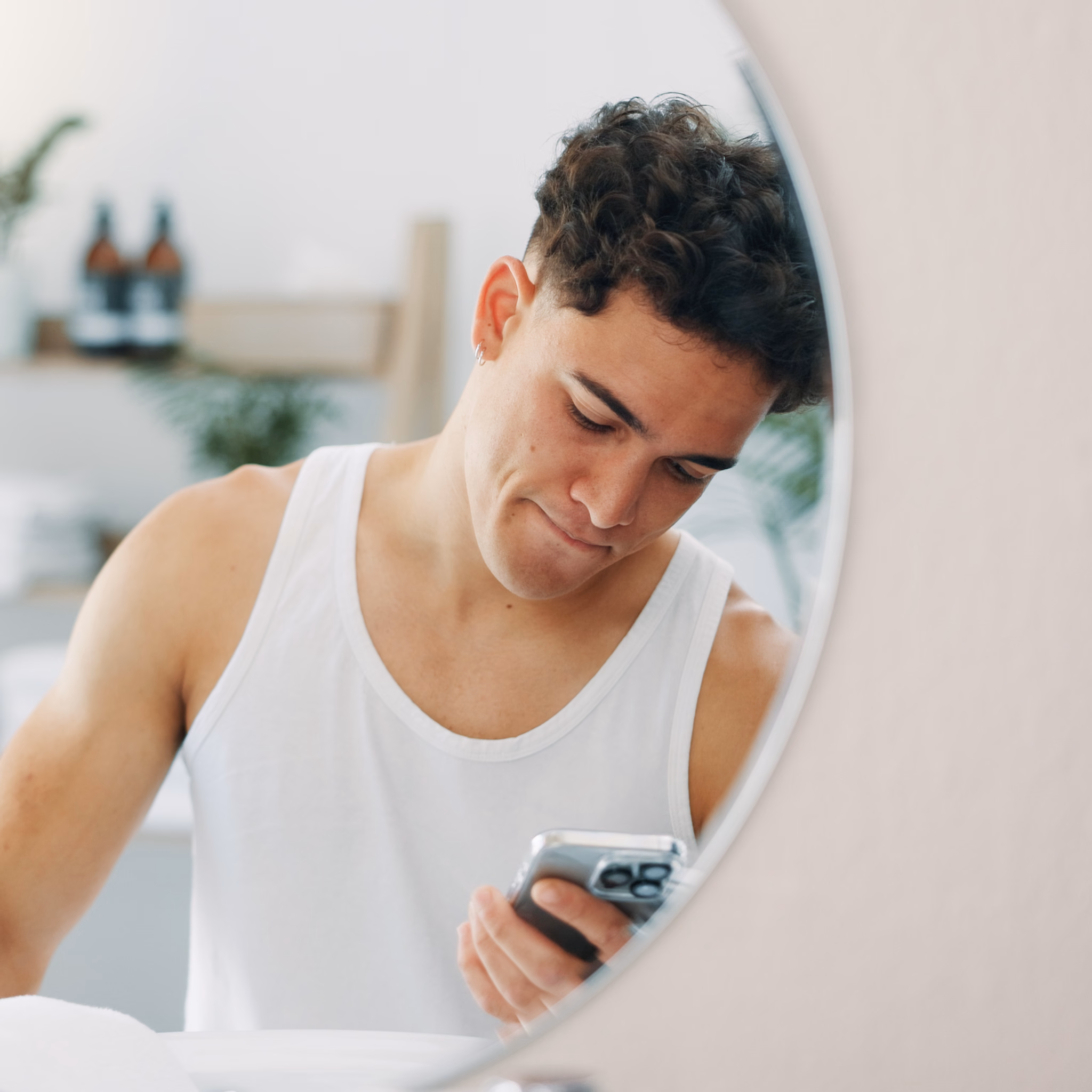 Mann steht im Unterhemd vor dem Spiegel und schaut ins Handy