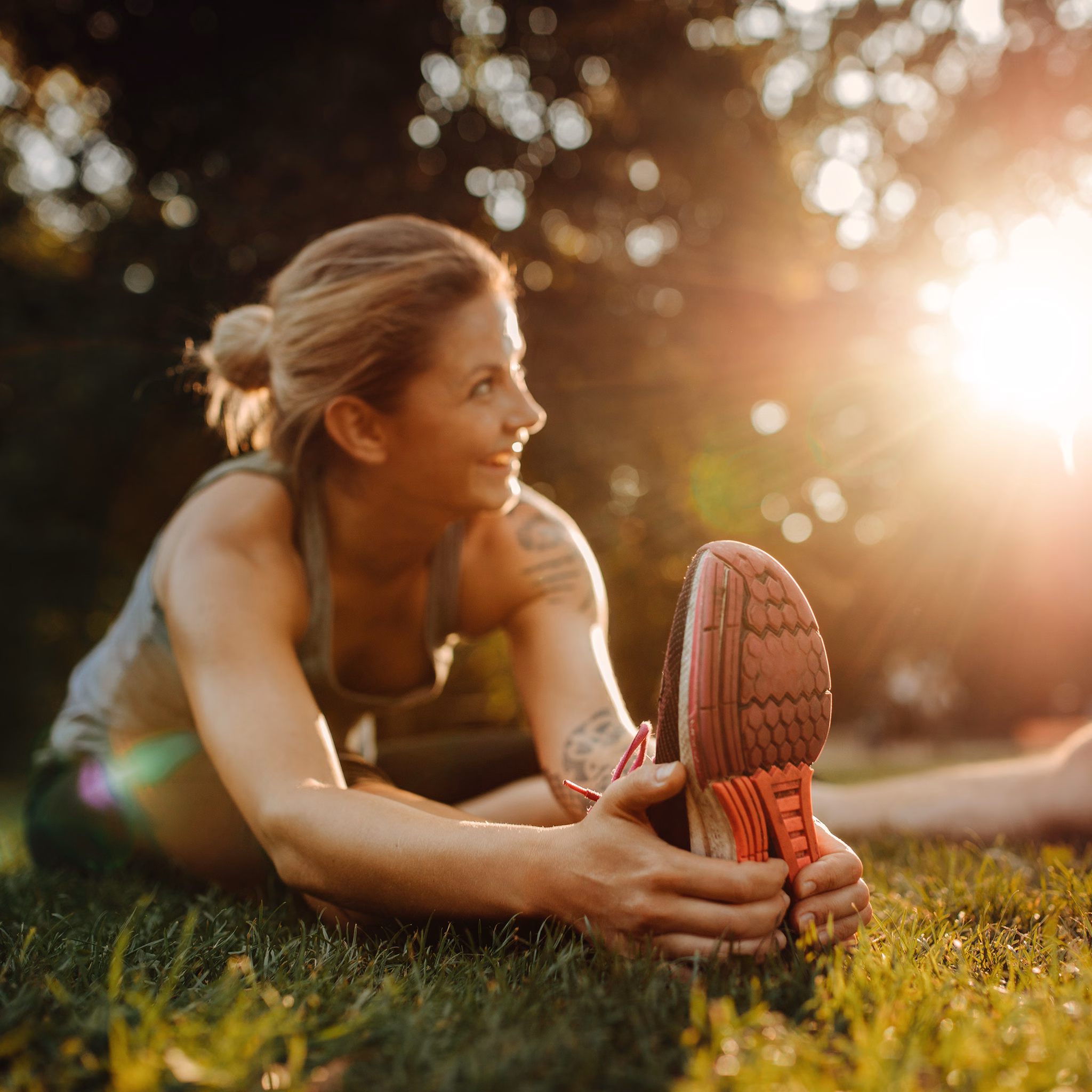 Sportliche Frau sitzt im Gras und dehnt ihr Bein