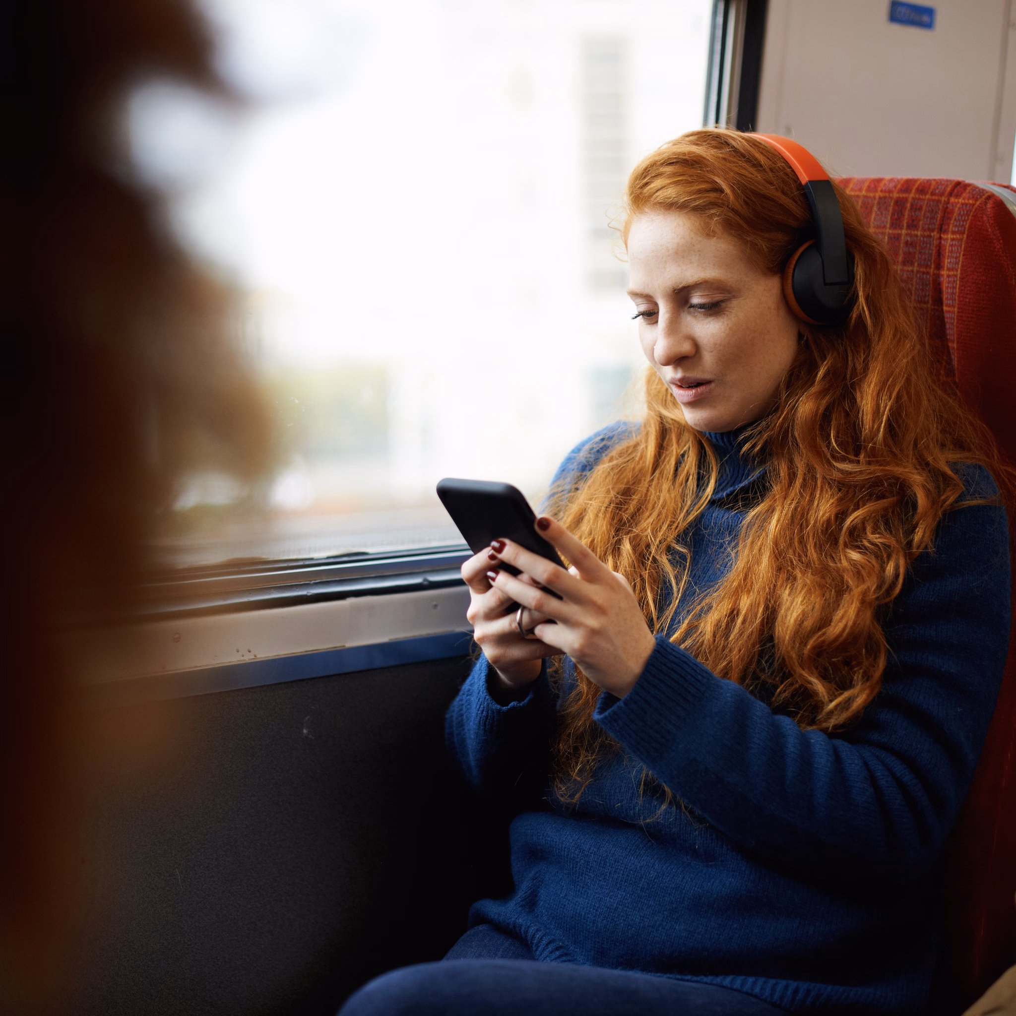 Junge Frau sitzt in der Bahn und schaut in ihr Handy