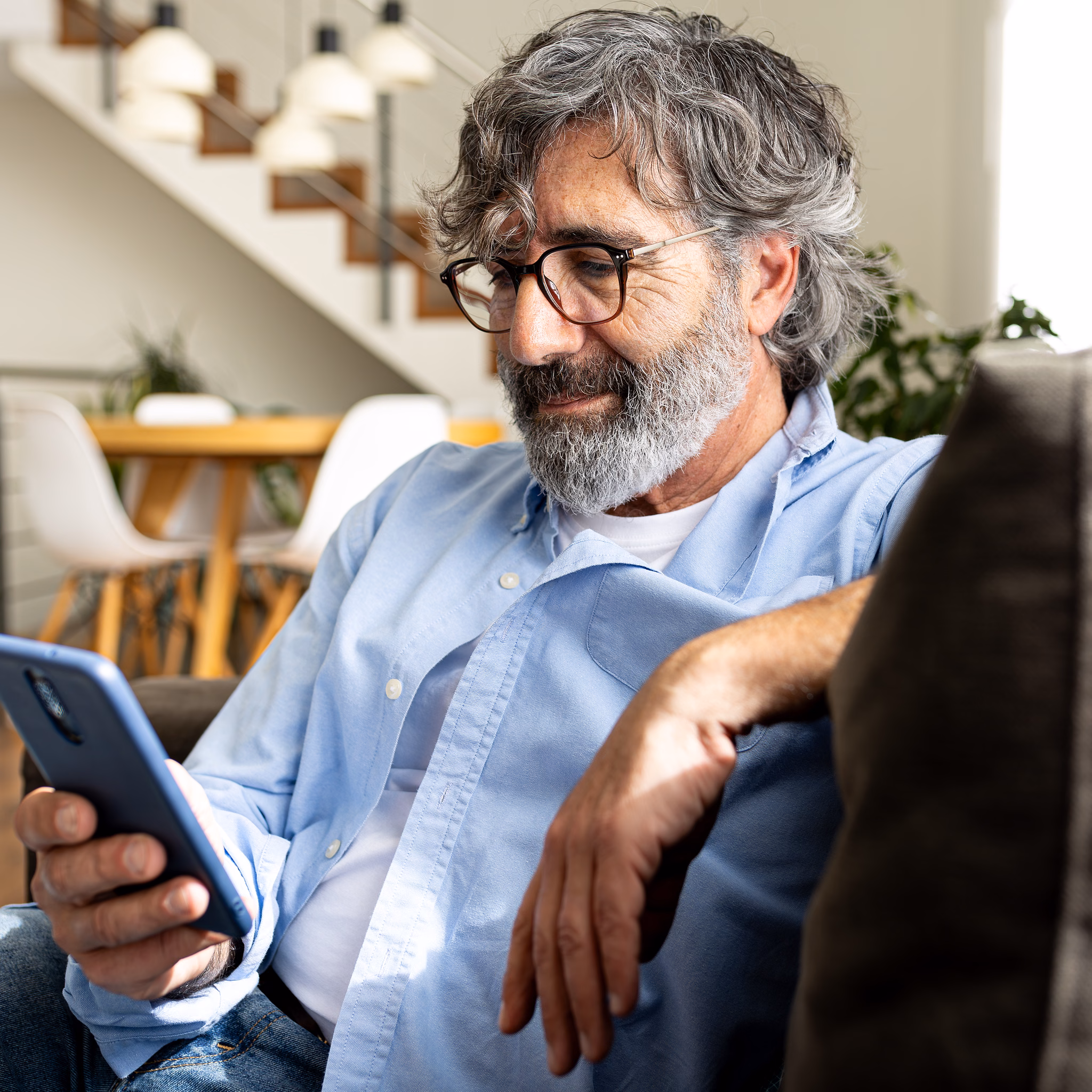 Mann sitzt auf dem Sofa und schaut auf sein Handy