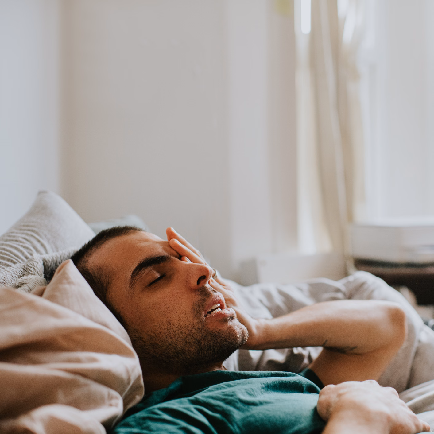 Junger Mann liegt mit Schmerzen im Bett
