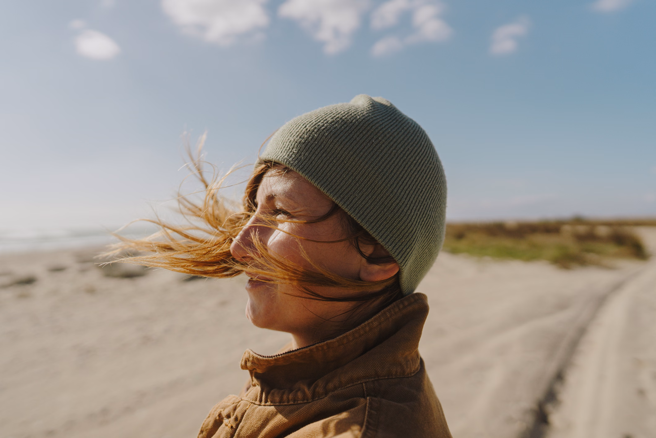 Frau mit Mütze steht am Strand bei Wind