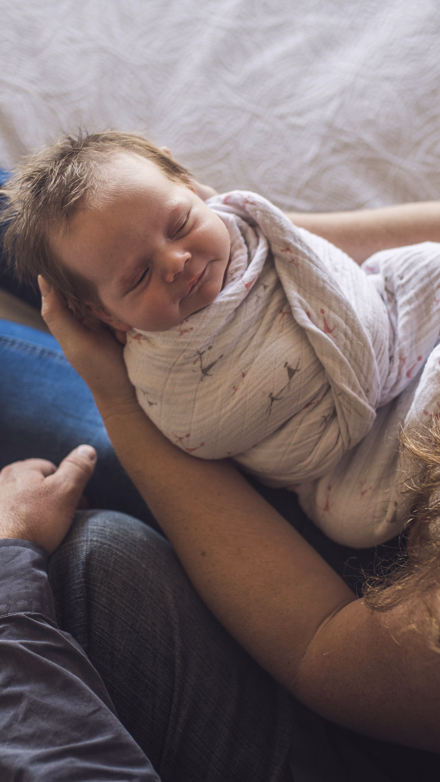 Baby liegt eingewickelt auf dem Schoß eines Paares.