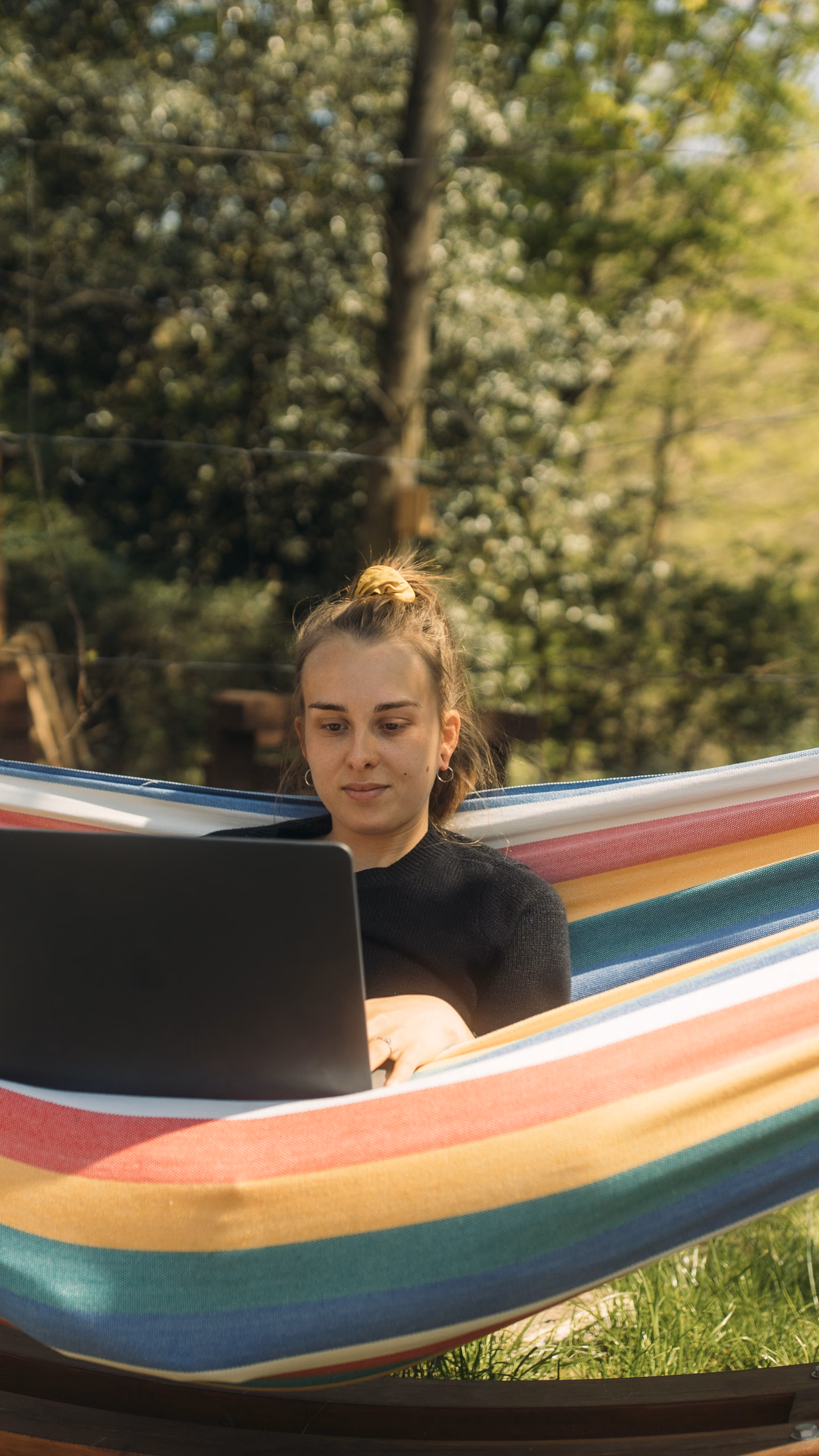 Junge Frau sitzt mit ihrem Laptop in einer Hängematte